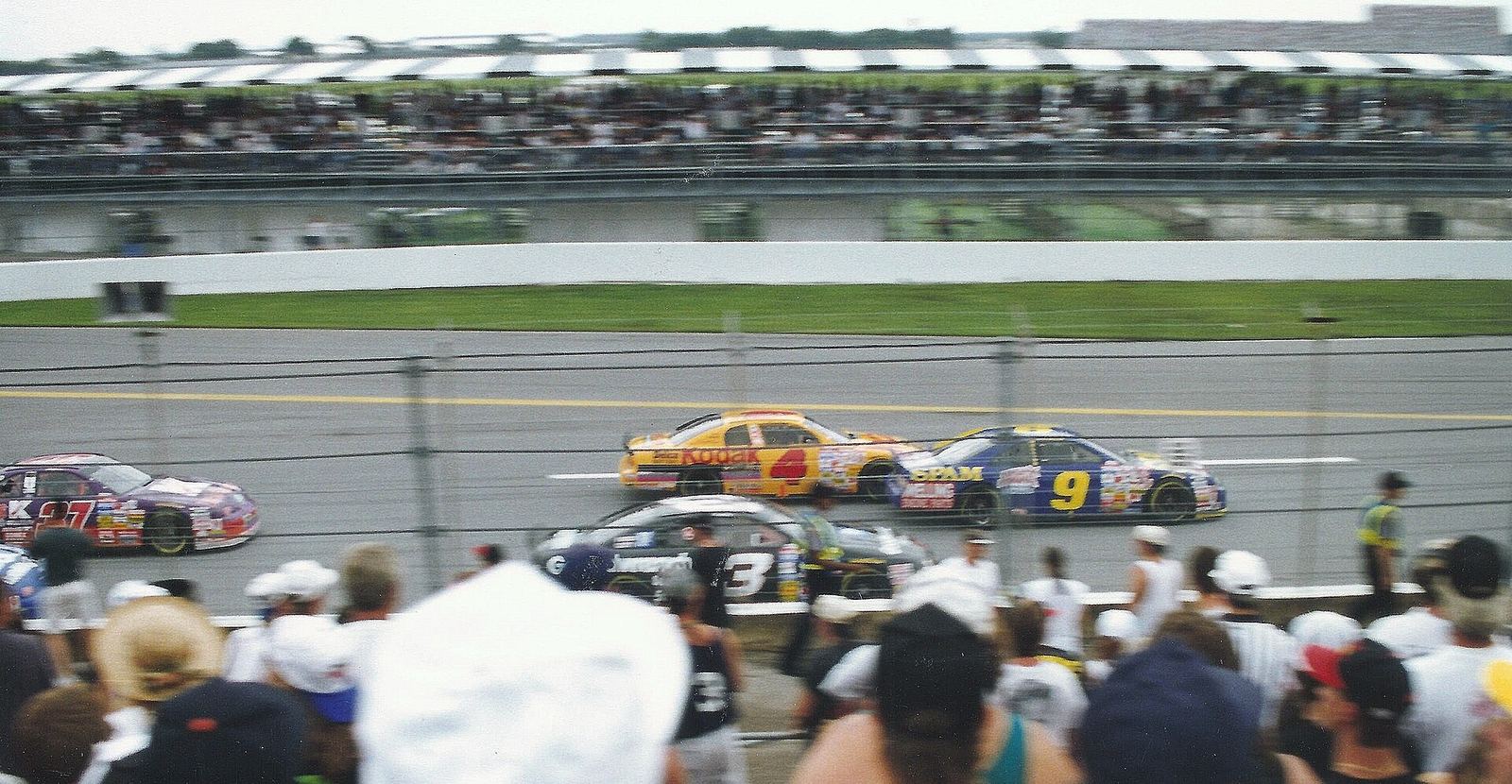 The yellow No. 4 Kodak car racing in a pack in front of a crowd during the 1996 Pepsi 400