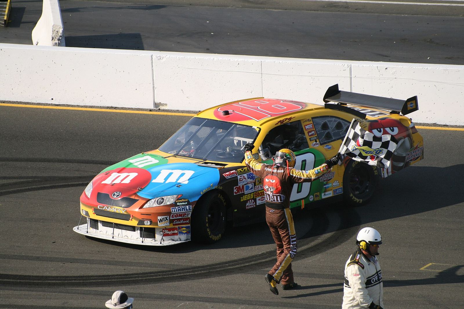 Kyle Busch walking back to his No. 18 M&M's Toyota with the checkered flag after winning at Infineon Raceway
